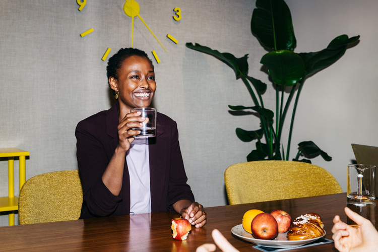 Leende kvinna som dricker ett glas vatten och äter ett äpple på jobbet