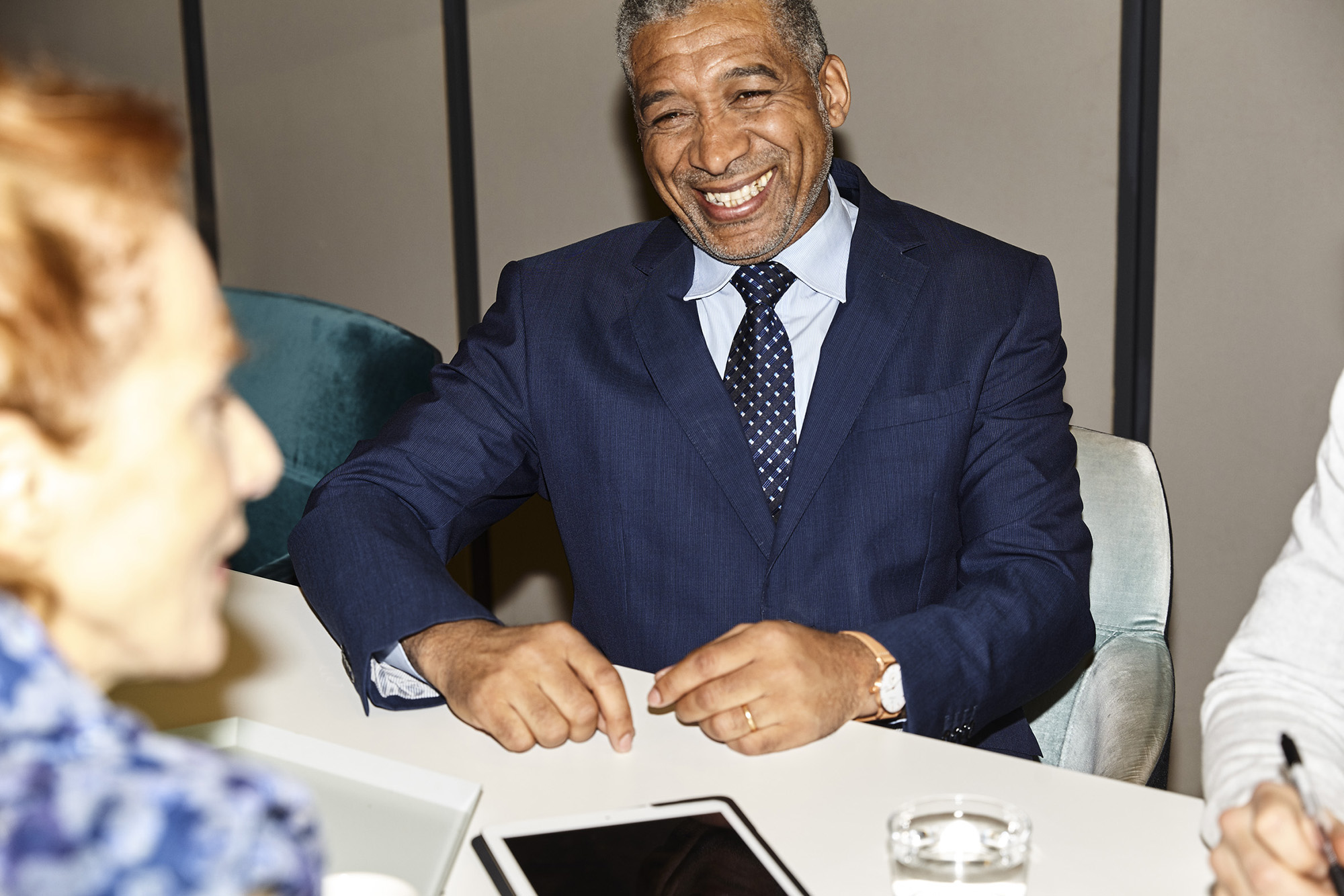 En leende äldre man i kostym vid konferensbord.