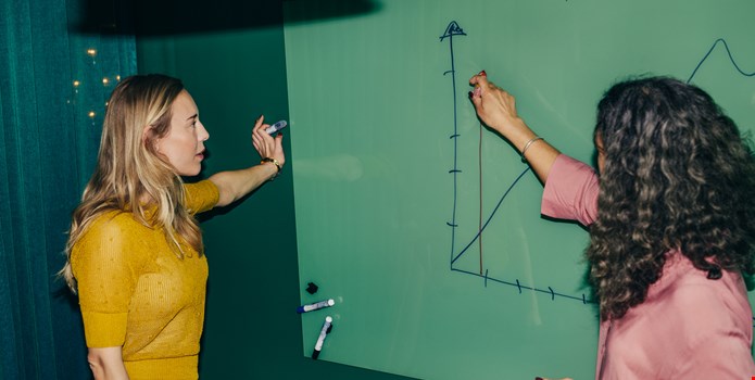Två personer tittar på en graf på en whiteboard.