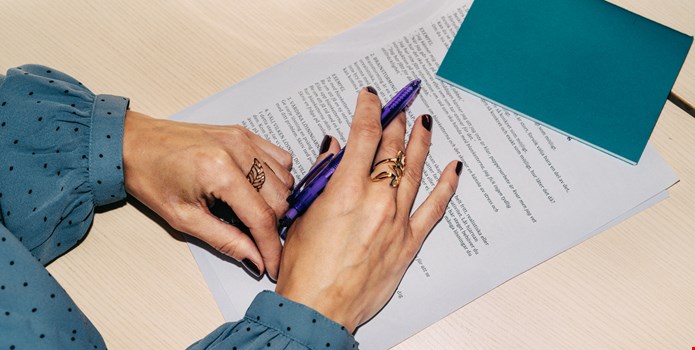 Ett par händer håller en penna över ett papper.