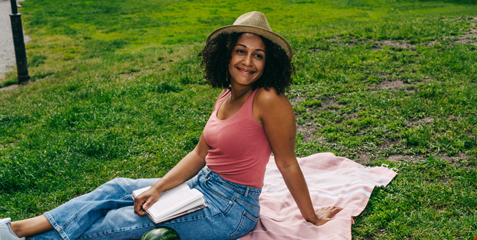 En kvinna njuter av semestern med en bok på en filt i gräset.
